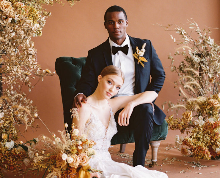bride leans against her groom as he sits in a velvet green chair