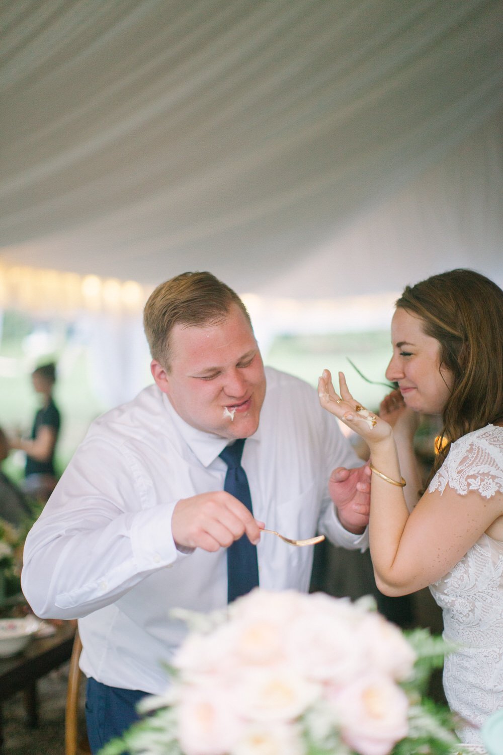bride and groom laugh as they feed each other cake