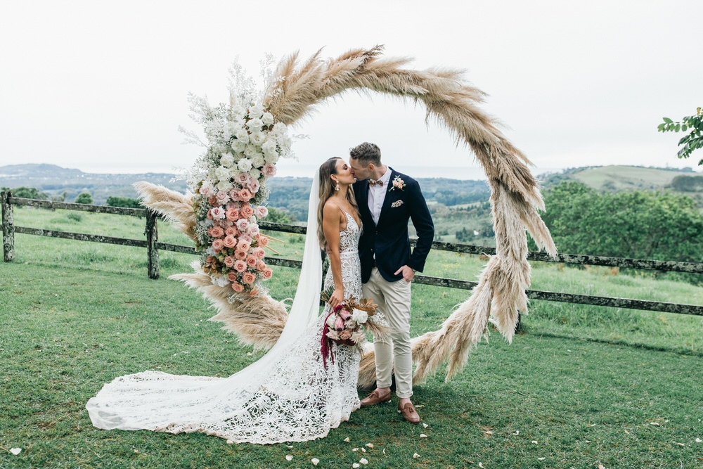 bride and groom kiss in front of circle pampas grass arch