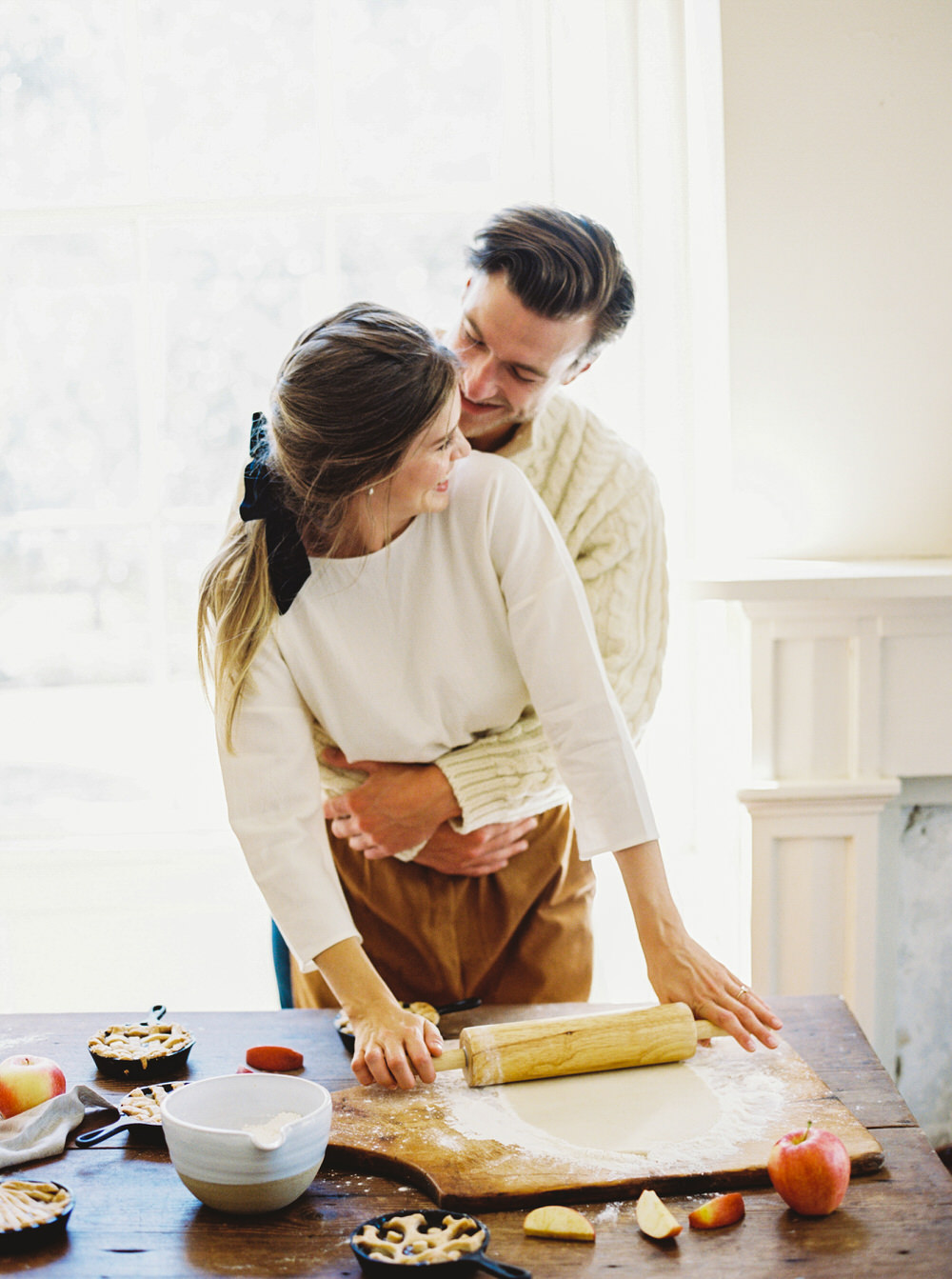 groom hugs his bride as they make apple pie