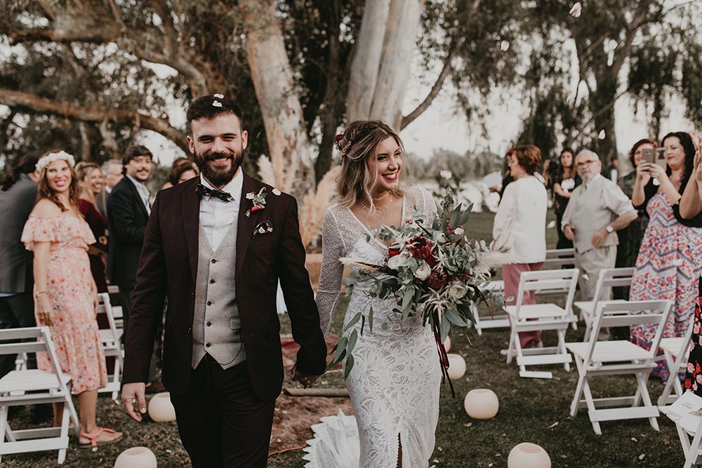 lace wedding dress and burgundy groom suit with pampas grass wedding backdrop
