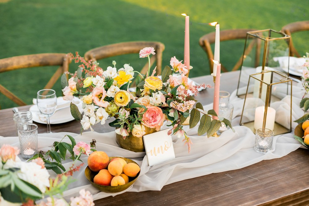 al fresco wedding tablescape with low wild centerpiece, thin wax candles and fruit bowls