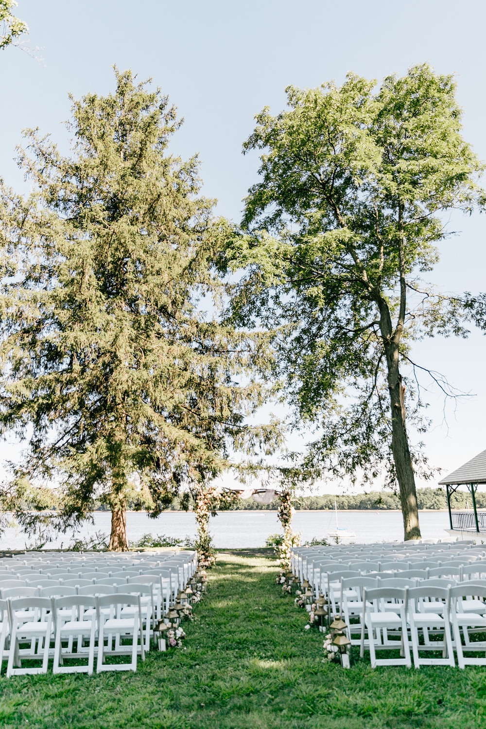 riverside wedding ceremony with white folding chairs and floral arch