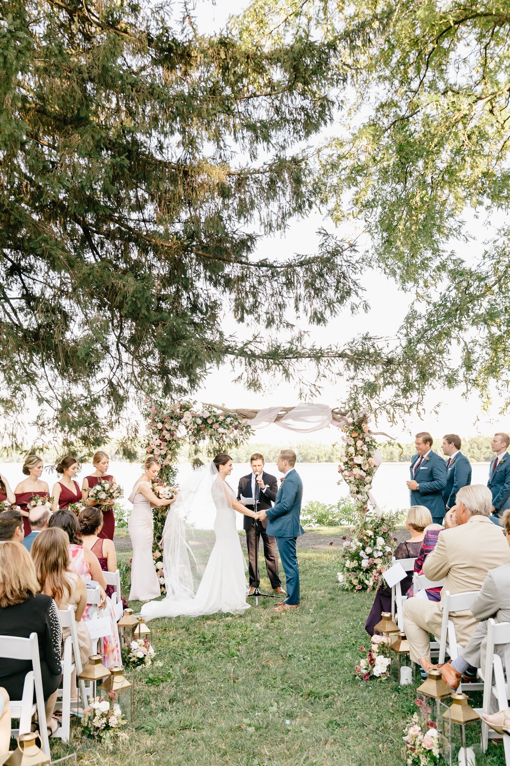 riverside wedding ceremony with white folding chairs and floral arch