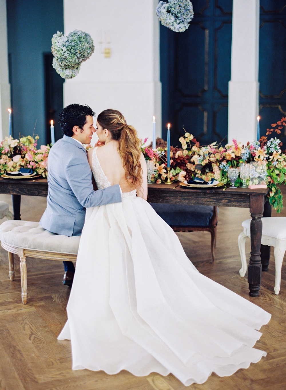 lace wedding dress with an overskirt and light blue groom suit with burgundy tie