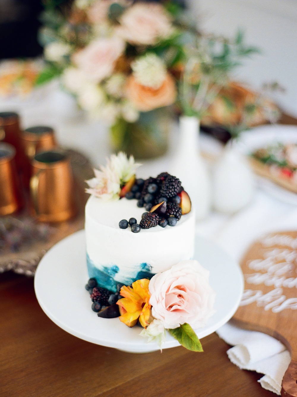 Blue and white cake topped with berries and accented with flowers