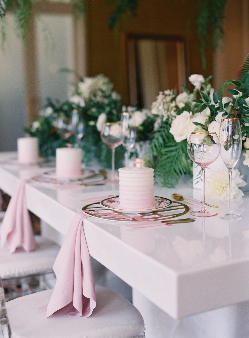 mini pink cake with rose colored wine glasses and a metallic copper charger
