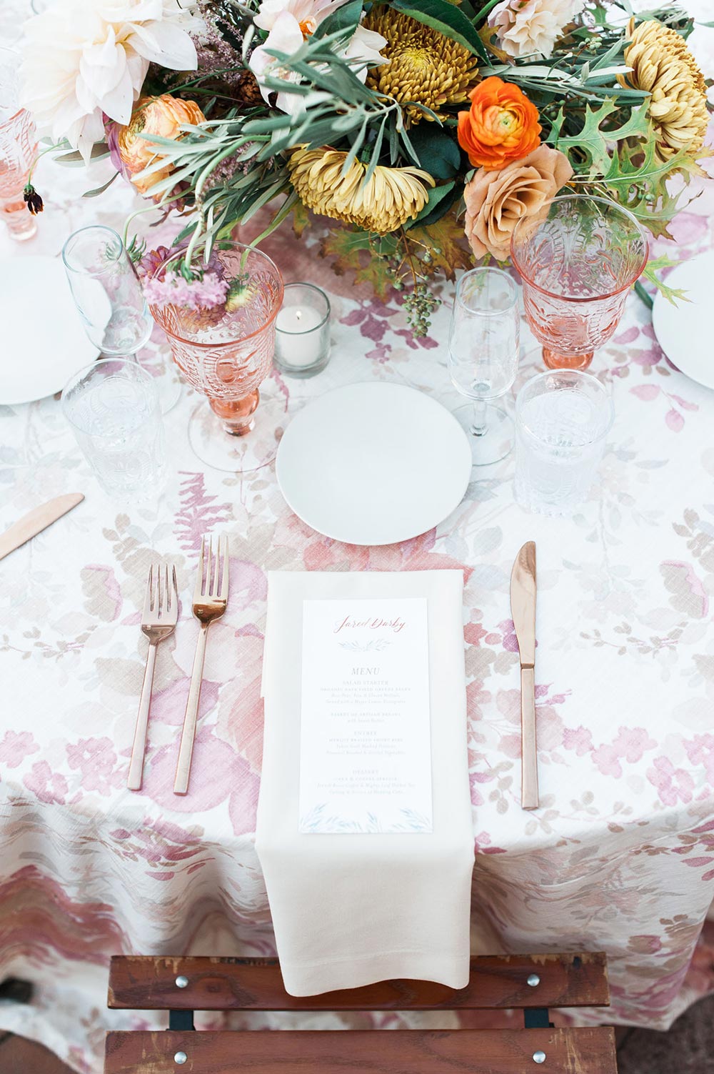 wedding place setting with pink floral table linen and copper utensils