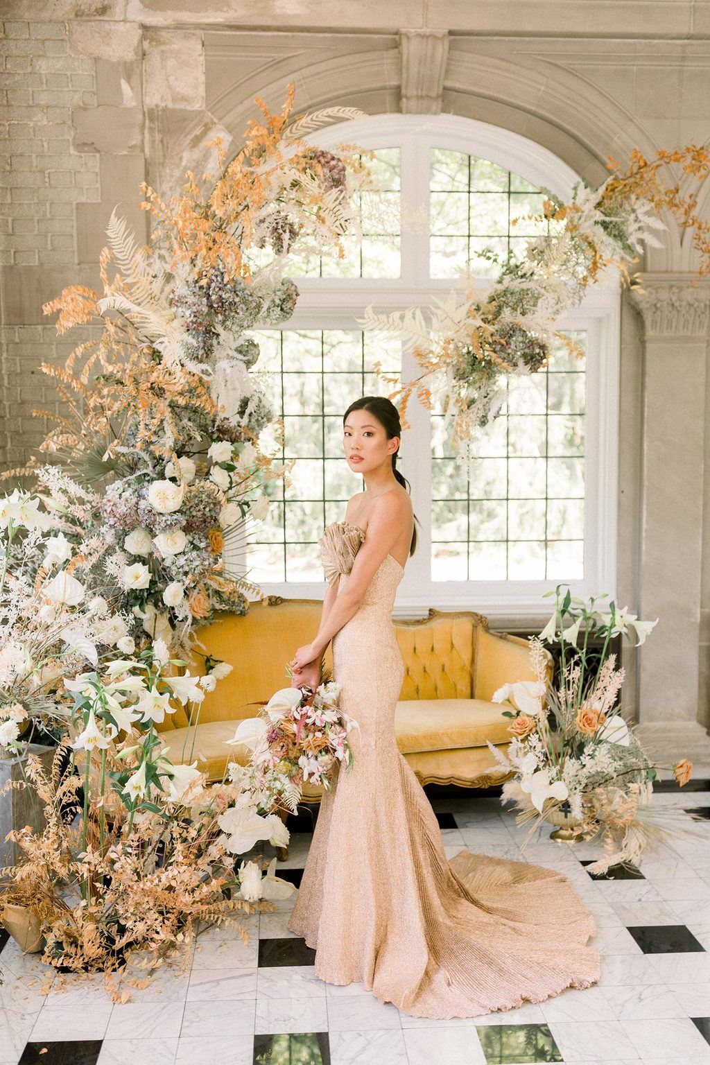 gold ruffled wedding dress with a vintage velvet sofa and wild, wispy floral installation